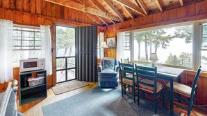 Een gezellig cabin interieur met houten wanden en plafond, een eettafel met stoelen, een magnetron en een raam met gordijnen.