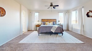 Un dormitorio con cama, ventilador de techo, reloj y ventana con cortinas.