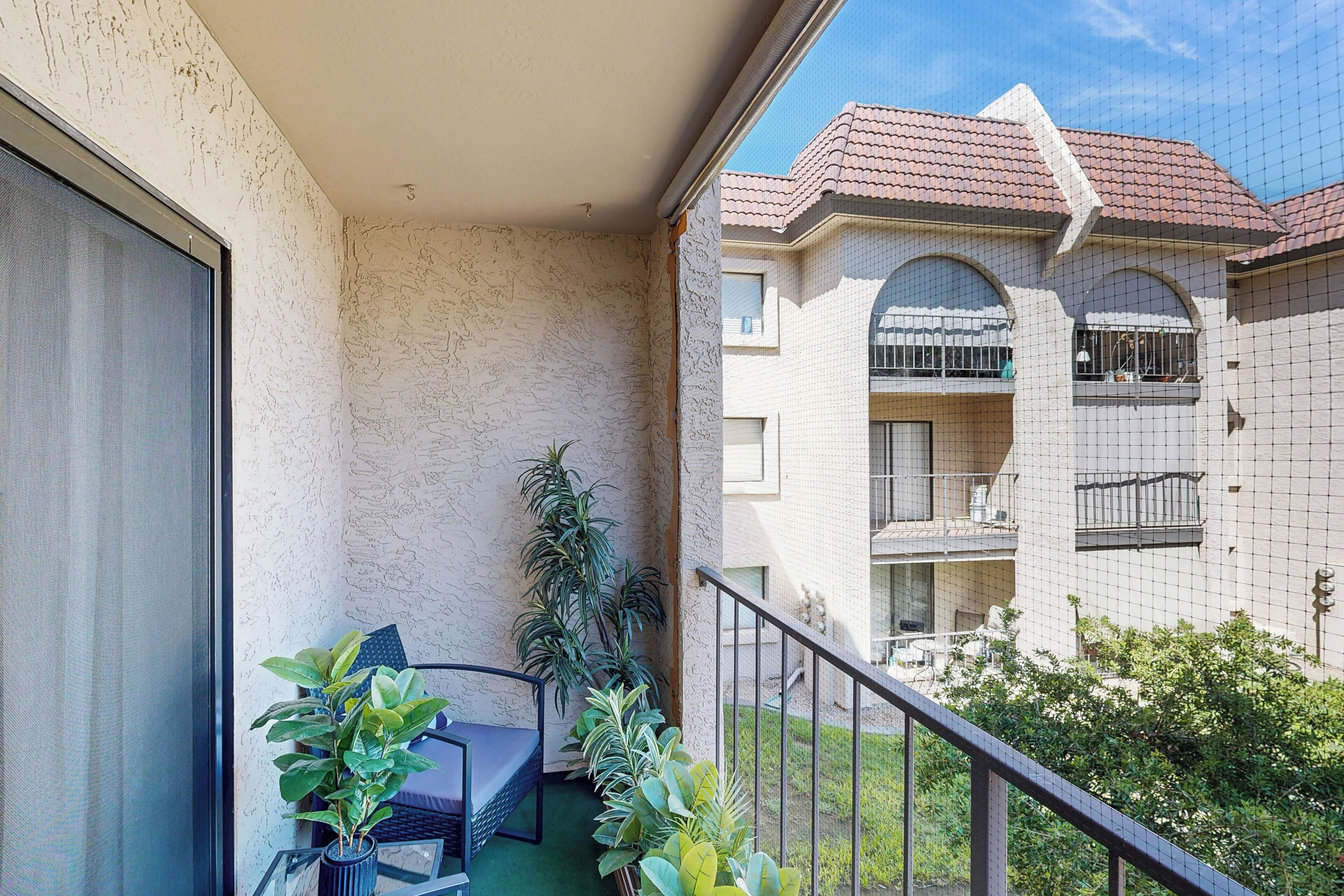 A balcony with a seating area, potted plants, and a view of neighboring buildings.