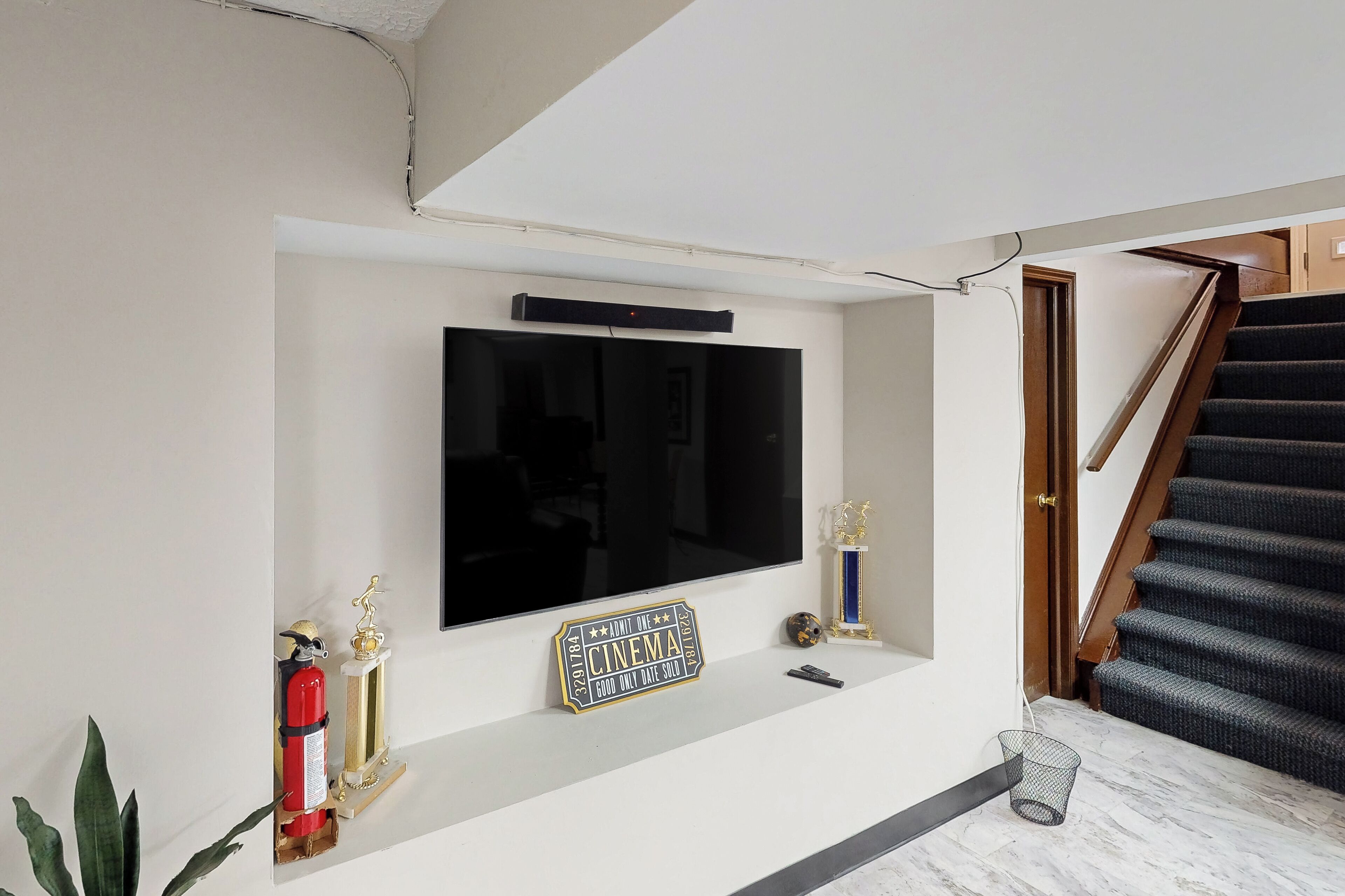 Una sala de estar con un televisor montado, un trofeo, un extintor y una escalera.