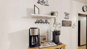 A coffee station with a coffee maker, a kettle, and a coffee mug on a wooden table. There are wall decorations including a coffee-themed sign and a shelf with a framed picture. - 3BR Private Stay w/ Game Room & Fireplace (Indianapolis)