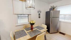 A dining area with a table set for four, a refrigerator, and a window with blinds. - 3BR Private Stay w/ Game Room & Fireplace (Indianapolis)