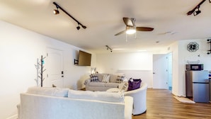 A modern living room with a sofa, a coffee table, and a ceiling fan. There is a door leading to another room and a refrigerator in the background. - Dog-friendly Apt w/ Fenced Yard in Winter Park (Winter Park)