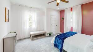 A bedroom with a bed, a bench, a ceiling fan, a door, and a window with curtains. - Modern Dallas Retreat 5 Mi to Dtwn: Pets Welcome (Dallas)