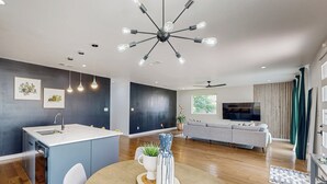 A modern kitchen with a central island, a dining area with a round table, and a living room with a sofa and TV. - Modern Dallas Retreat 5 Mi to Dtwn: Pets Welcome (Dallas)