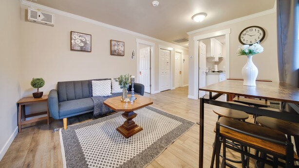 Een moderne woonkamer met een donkerblauwe bank, een houten salontafel, en een eetgedeelte met een houten tafel en stoelen.