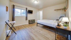 Een slaapkamer met een bed, nachtkastje, lamp en een klein plankje met een plantje.