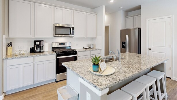 Una cocina moderna con armarios blancos, encimera de granito, electrodomésticos de acero inoxidable y una pequeña isla con taburetes de bar.