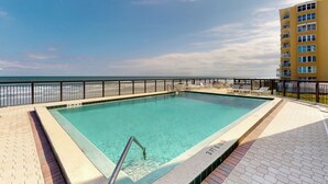 Una piscina rectangular con una escalera metálica, rodeada por un patio de baldosas y una barandilla de metal negro.