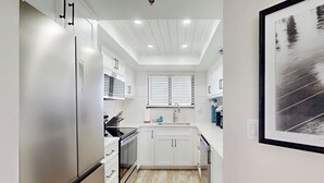 Una cocina moderna con armarios blancos, un refrigerador de acero inoxidable, un horno empotrado y una ventana con persianas.