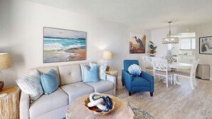 Una sala de estar con sofá, sillón azul y una mesa de comedor con sillas.