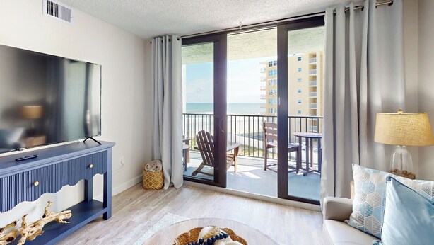 Una habitación de hotel moderna con un televisor grande, un balcón con vista al mar y un sofá con lámpara.