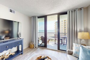 A modern hotel room with a large TV, a balcony with a view of the sea, and a sofa with a lamp. - 1BR Stylish Condo w/ Ocean Views, Pool (New Smyrna Beach)