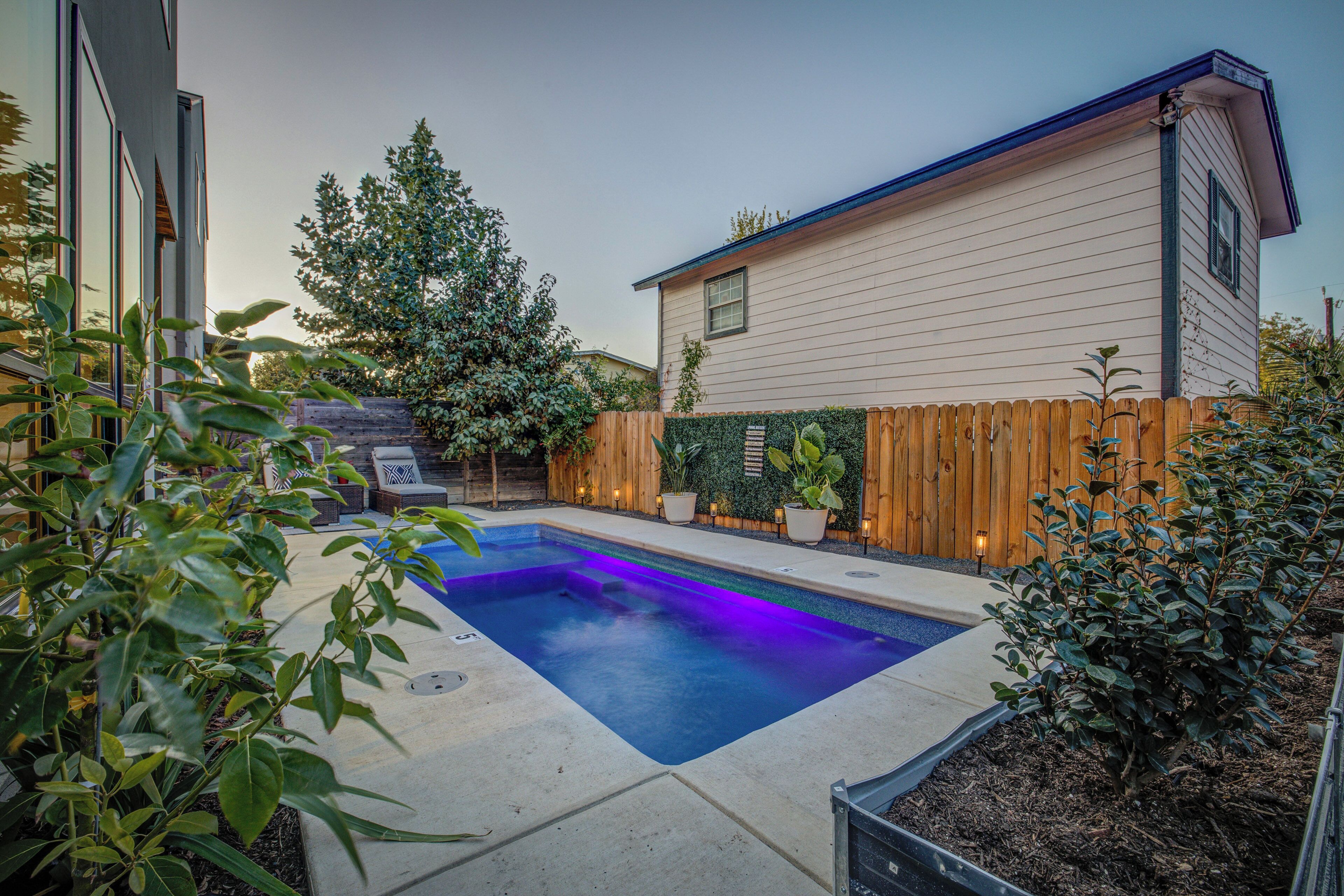 A backyard with a swimming pool, wooden fence, and potted plants.