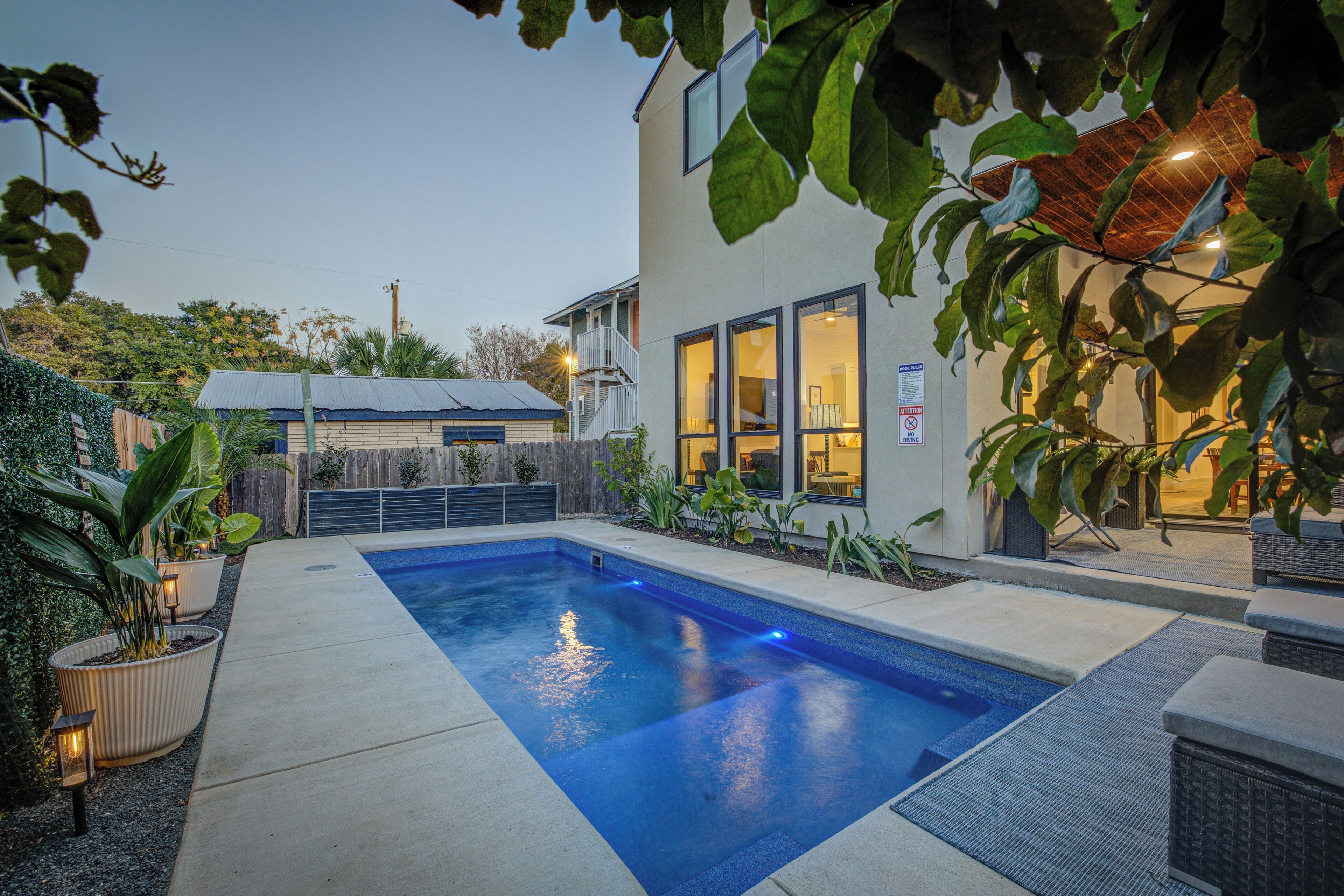A modern house with a swimming pool, surrounded by potted plants and outdoor furniture.