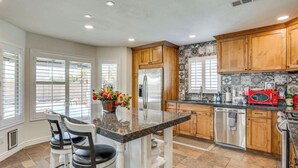 A kitchen with granite countertops, wooden cabinets, a stainless steel refrigerator, and a red microwave. - 4BR Home w/ Private Pool, Patio & Grill (Glendale)