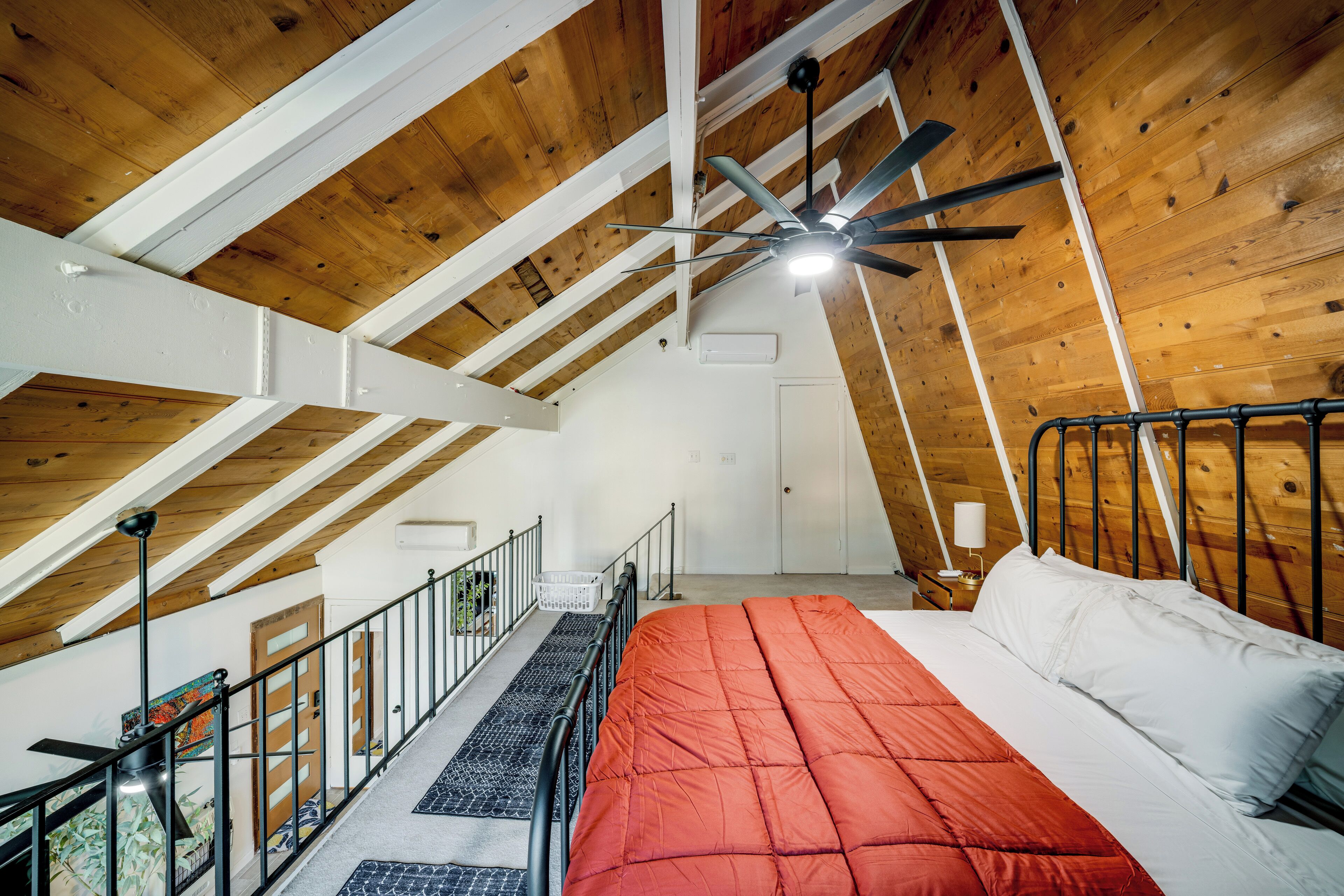 A bedroom with a sloped ceiling, a bed with a red and white comforter, a ceiling fan, and a window.