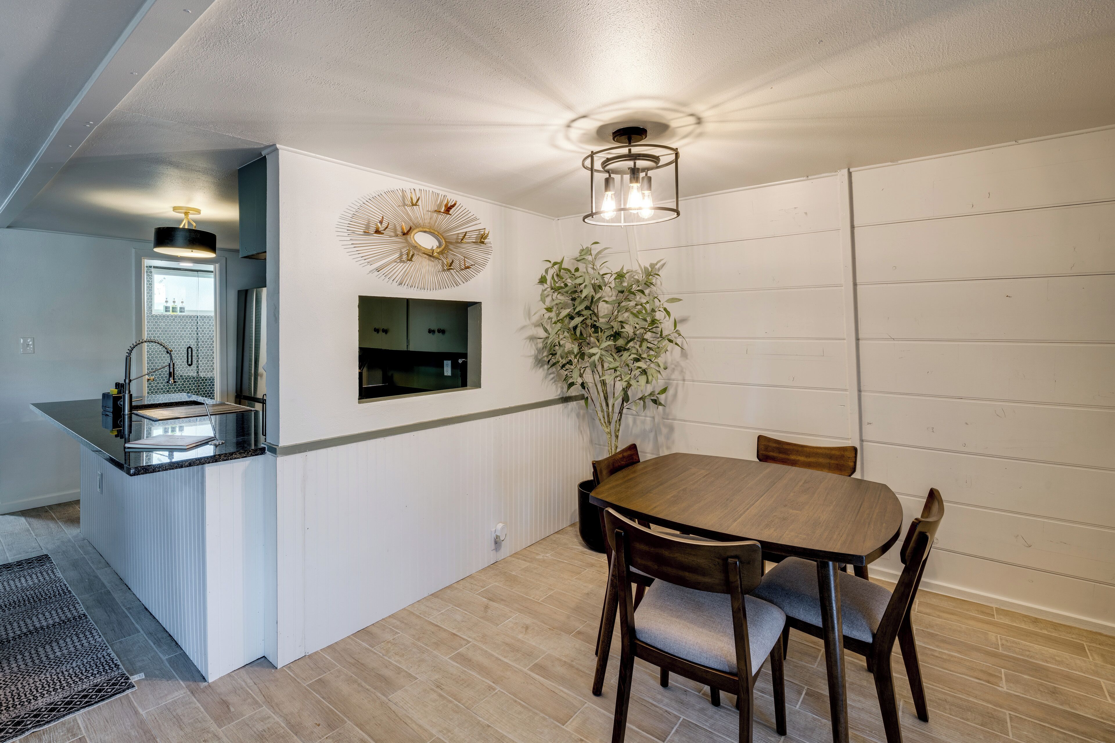 Un comedor con mesa y sillas de madera, una planta en maceta y una lámpara colgante.