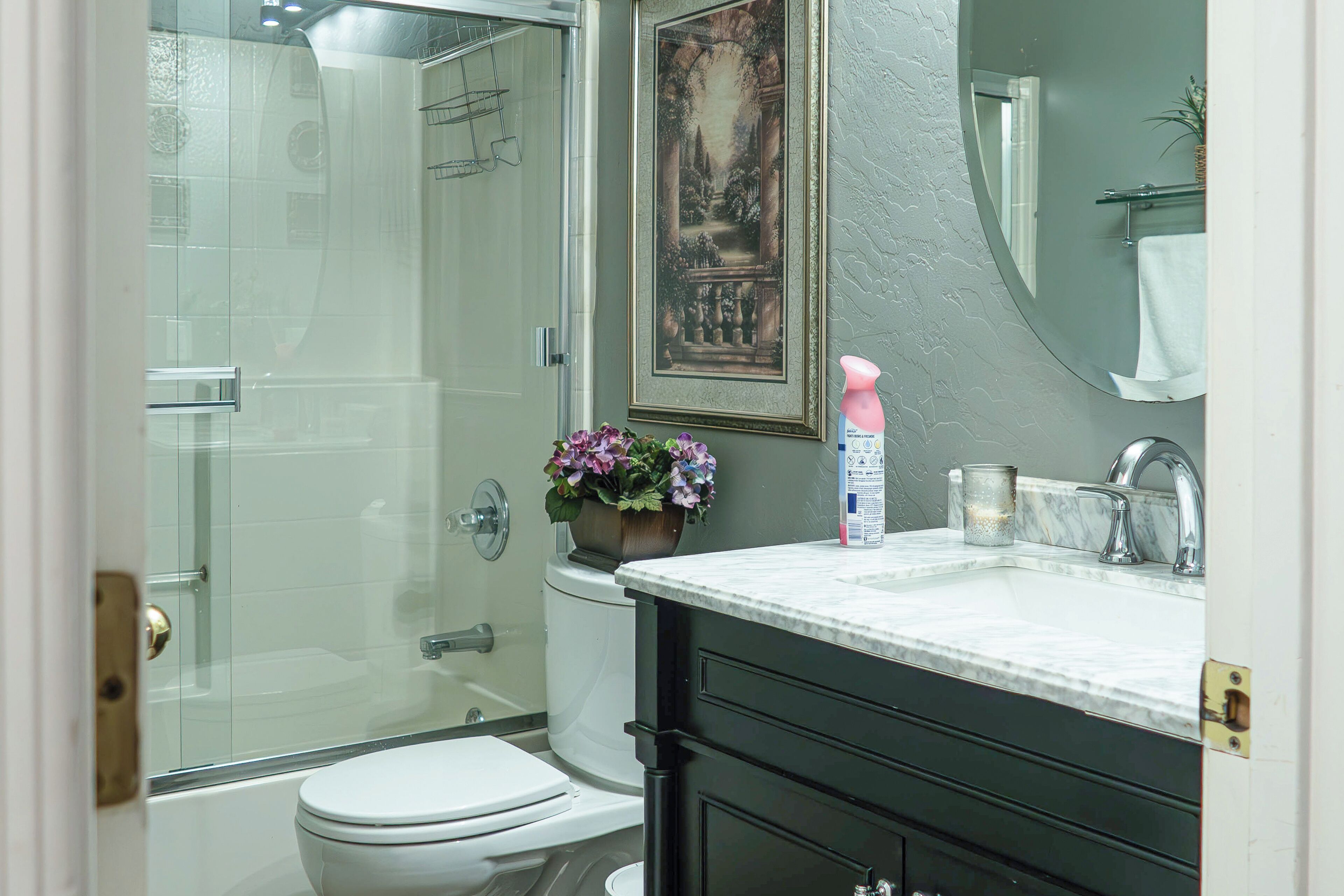 Une salle de bain dotée d’une douche à parois de verre, de toilettes, d’un lavabo avec un plan de travail en marbre et d’un tableau encadré au-dessus du miroir.