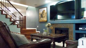 A living room with a staircase, a flat-screen TV, a fireplace, and a framed picture of a lion. - Group-ready Glendale Oasis w/ Pool Grotto + Slide (Glendale)