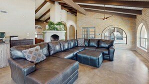 A spacious living area with a large L-shaped leather sectional sofa, exposed wooden beams, brick walls, and a fireplace. - Peaceful, Spacious, Luxury Backyard, Putting Green (Scottsdale)
