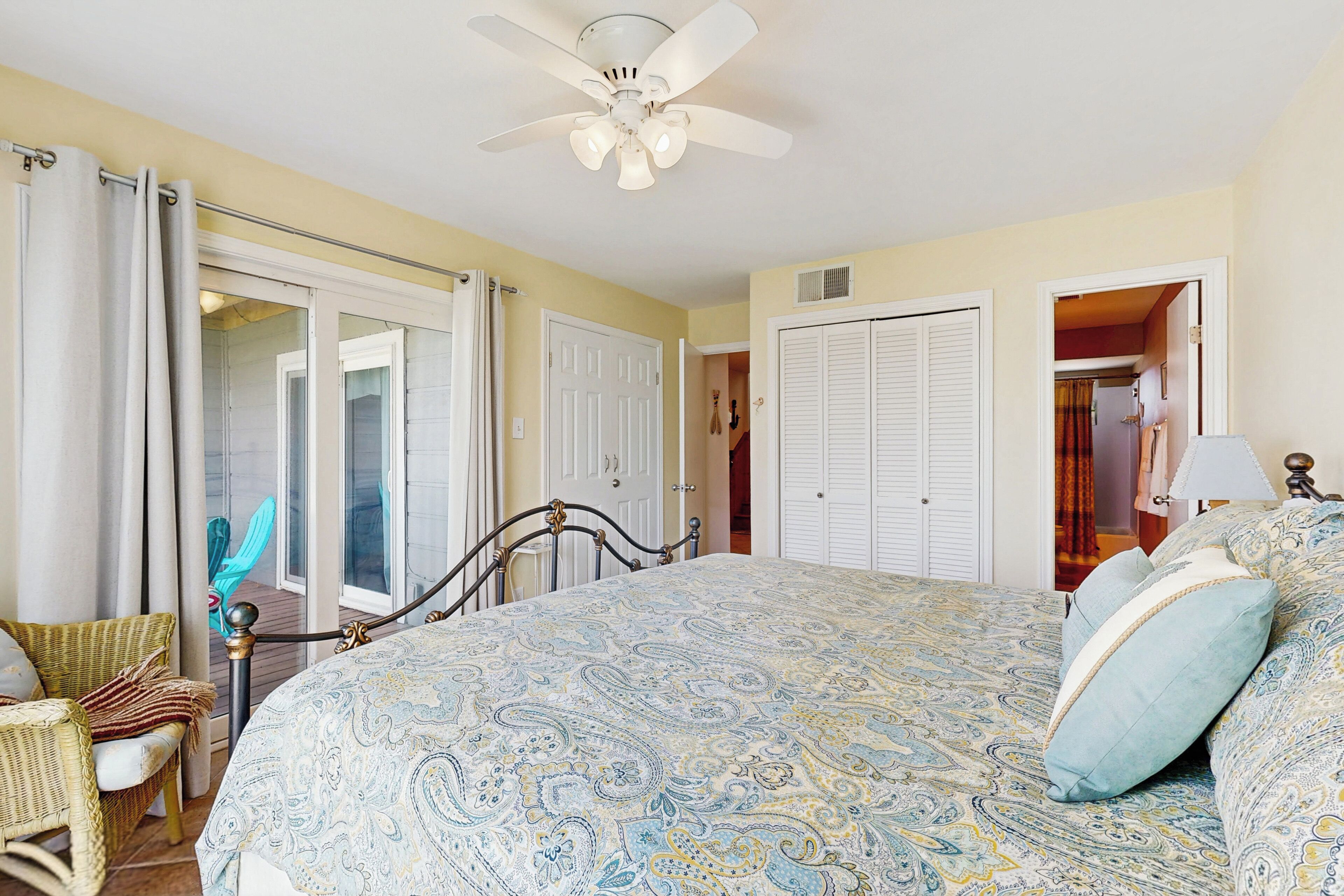 A bedroom with a large bed, a ceiling fan, and a view of a balcony.