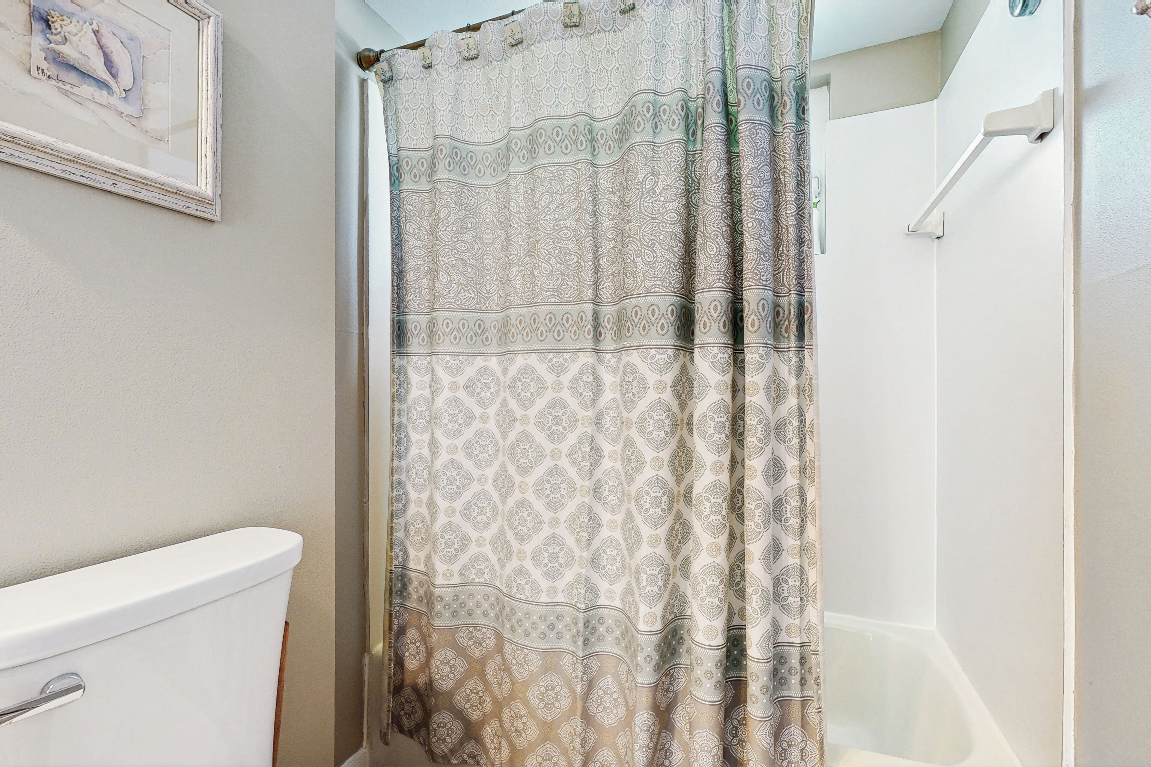 Une salle de bain avec un rideau de douche à motifs, des toilettes blanches et un tableau encadré au mur.