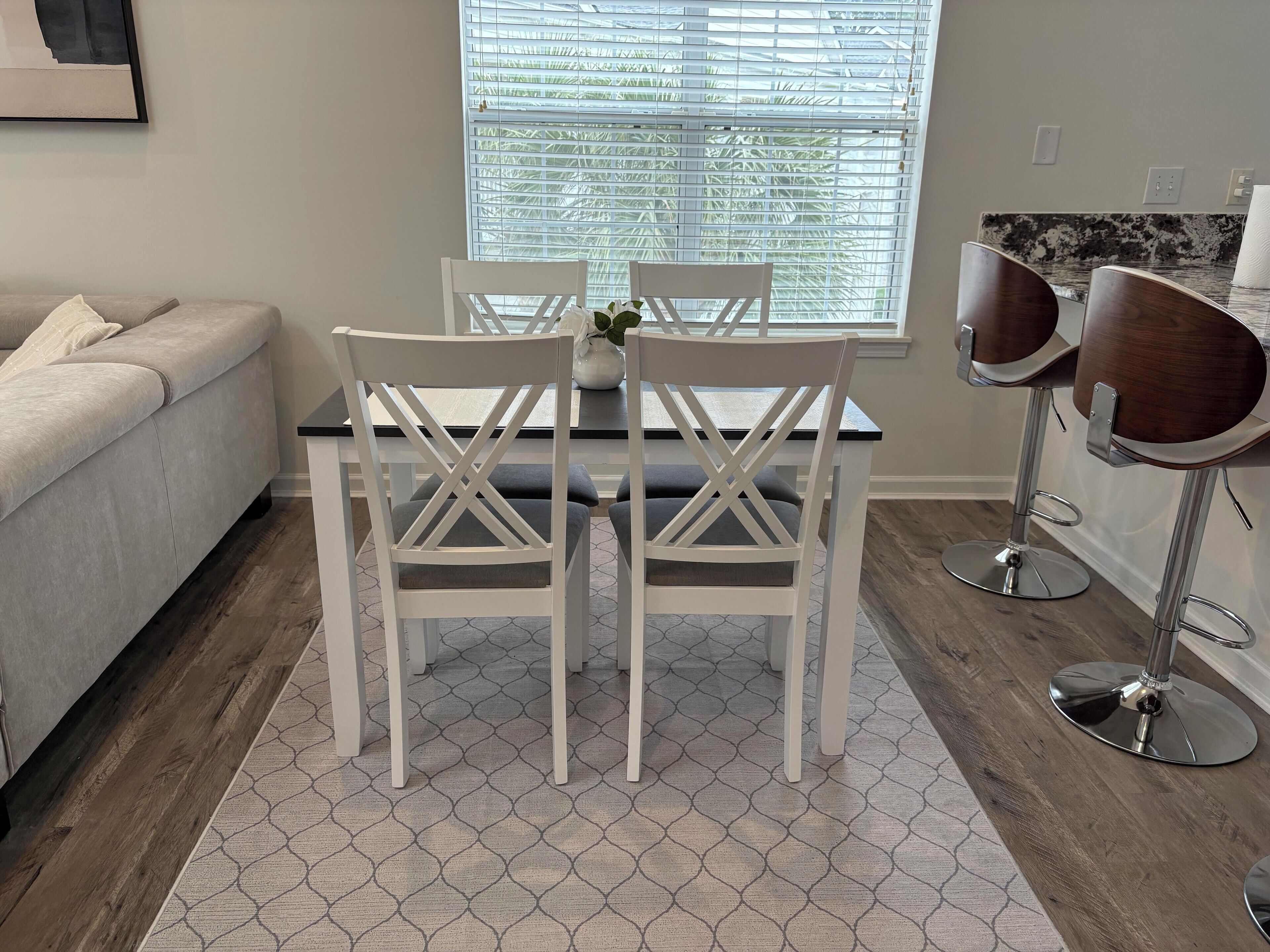 A dining area with a table and four chairs, a sofa, and a window with blinds.