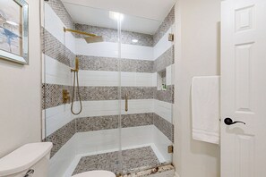 Une salle de bain avec une douche à parois de verre, des carreaux blancs et des toilettes blanches.