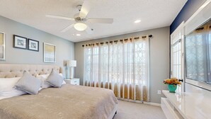 Un dormitorio con una cama grande, un ventilador de techo y una ventana con cortinas.