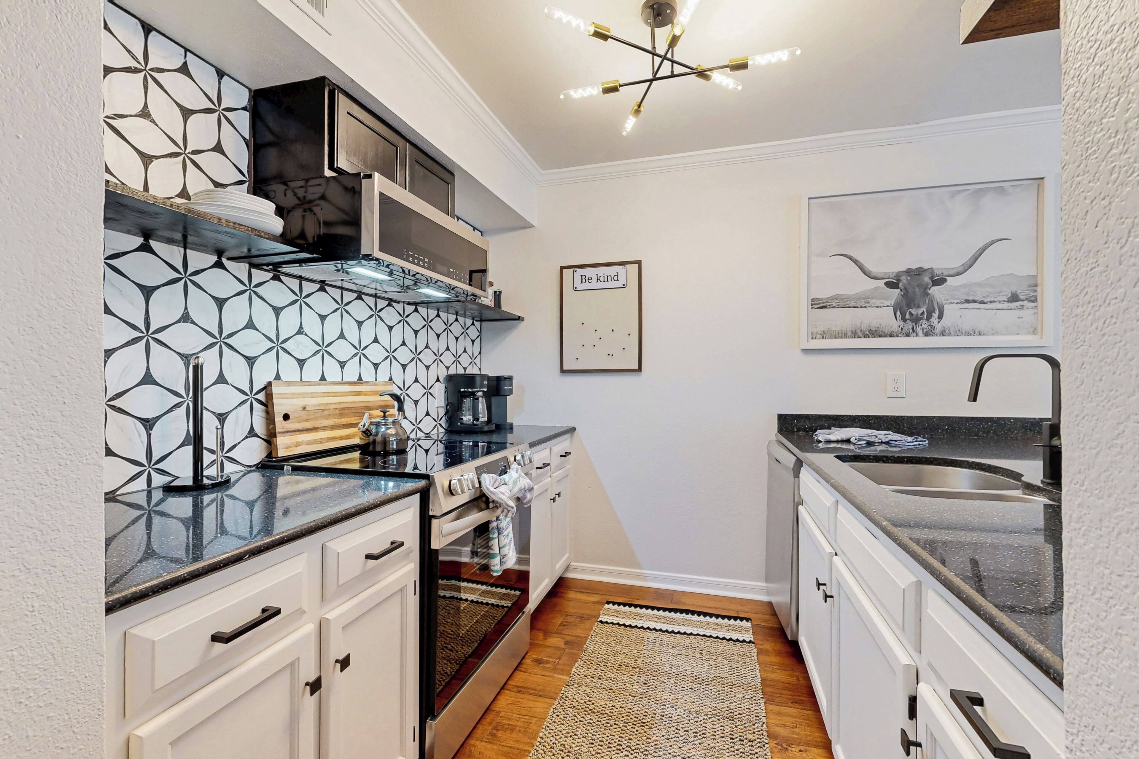 A compact kitchen with white cabinets, a black countertop, a coffee maker, and a hanging light fixture.
