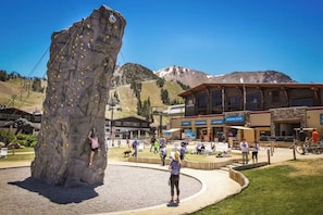 Uma grande parede de escalada com uma pessoa a escalar, cercada por um edifício com a placa Adventure Center.