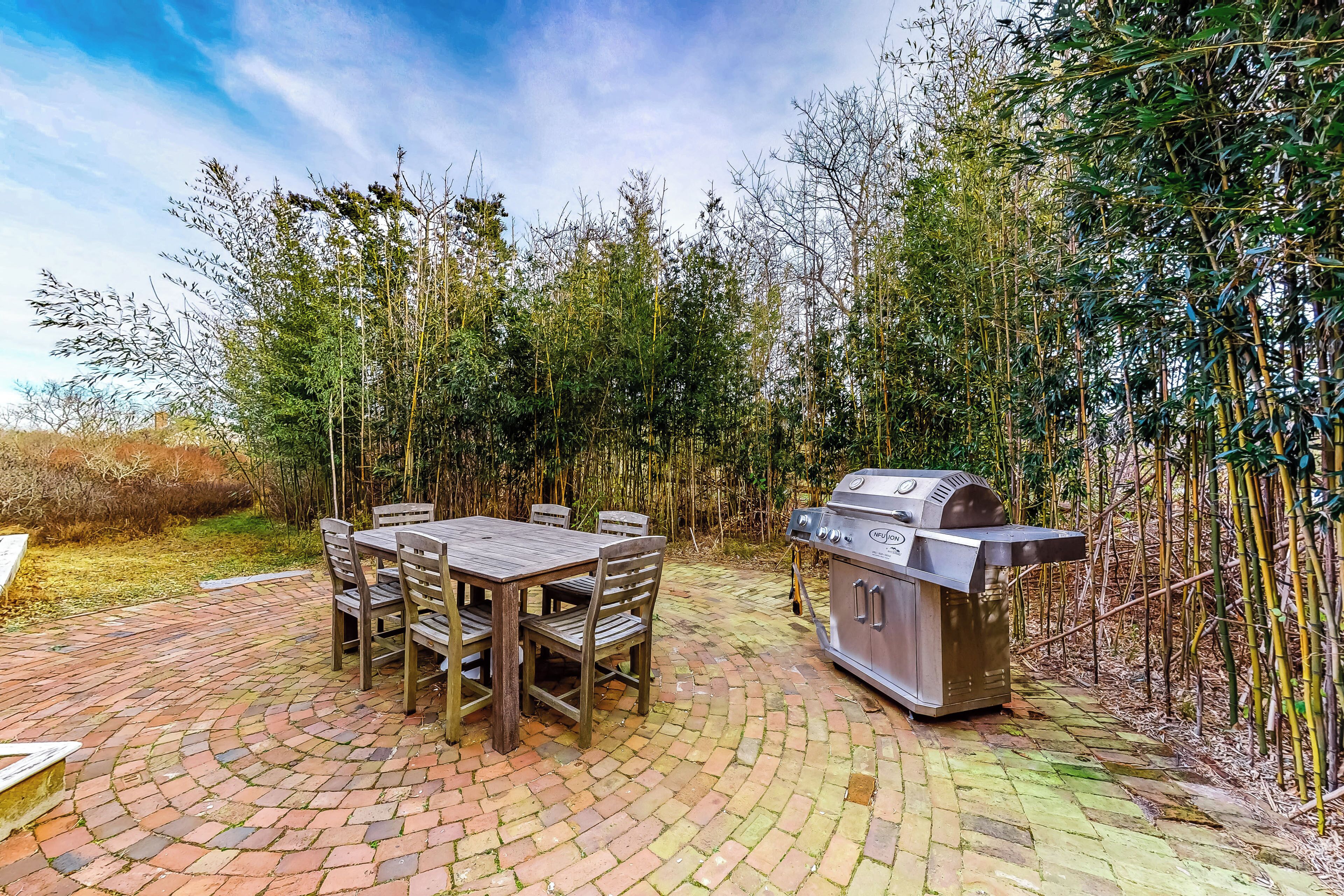 An outdoor patio with a brick floor, a wooden table with chairs, and a built-in grill.