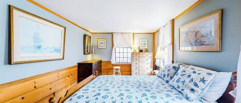 A bedroom with a wooden headboard, a bed with a blue and white patterned bedspread, a dresser, a nightstand, and two framed pictures on the wall.