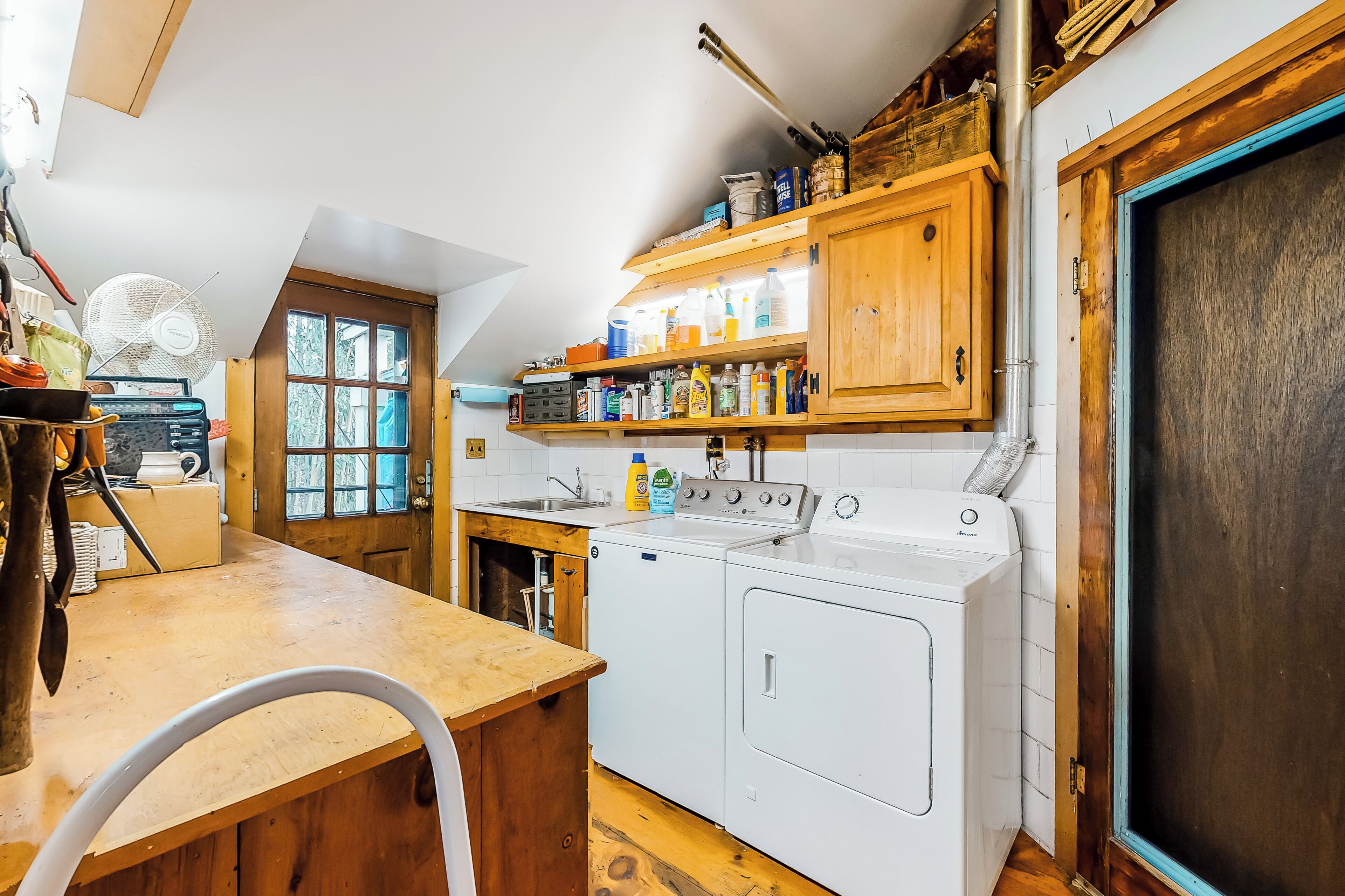 A laundry room with a washing machine, dryer, and shelves with cleaning supplies.