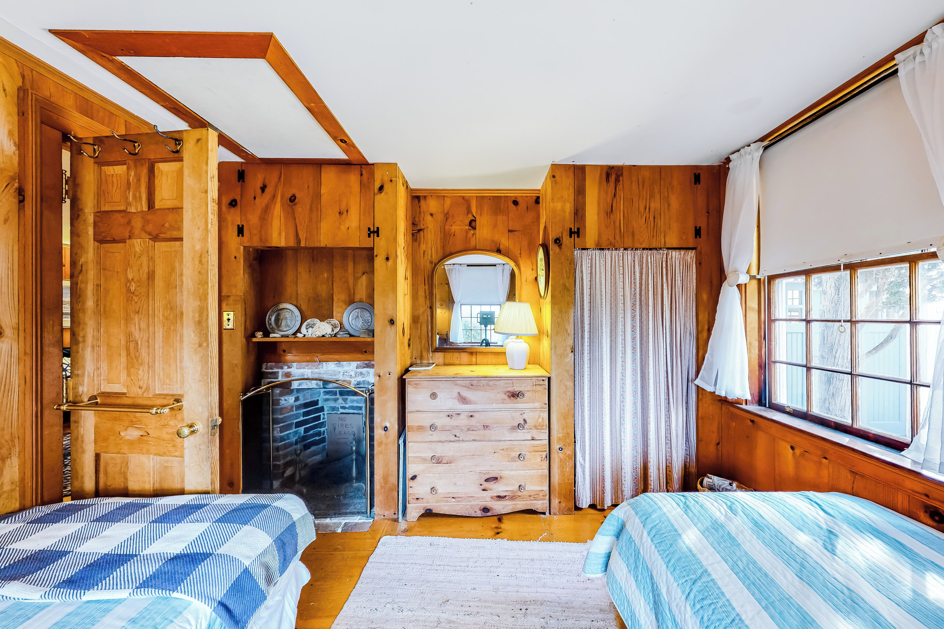 Ein Zimmer mit Holzboden, zwei Betten, einem Schminktisch, einem Spiegel und einem Fenster mit Vorhängen.