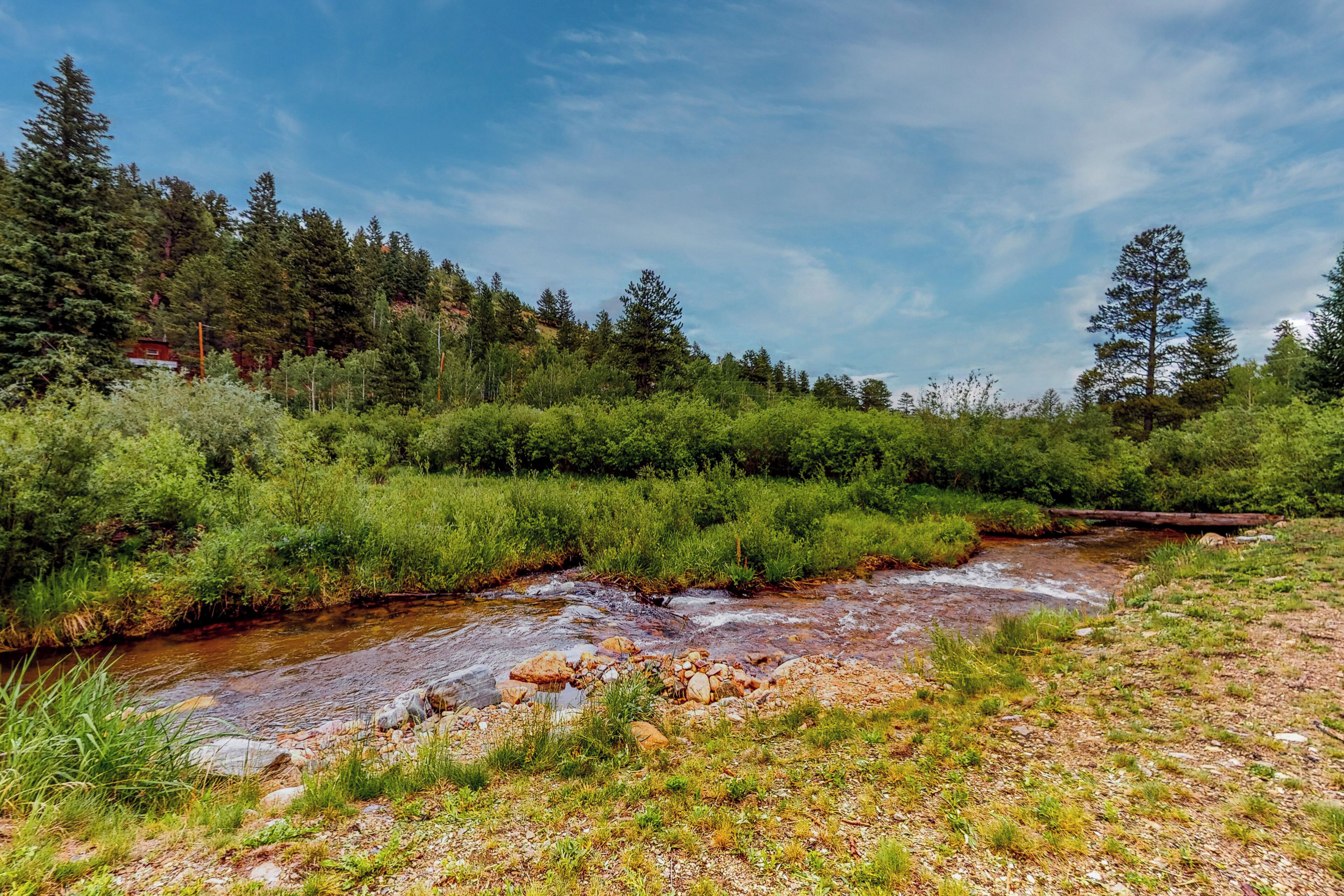 A natural landscape with a flowing river, dense greenery, and a forested hillside.