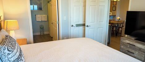 A bedroom with a large bed, a TV, a dresser, and a door leading to a bathroom.