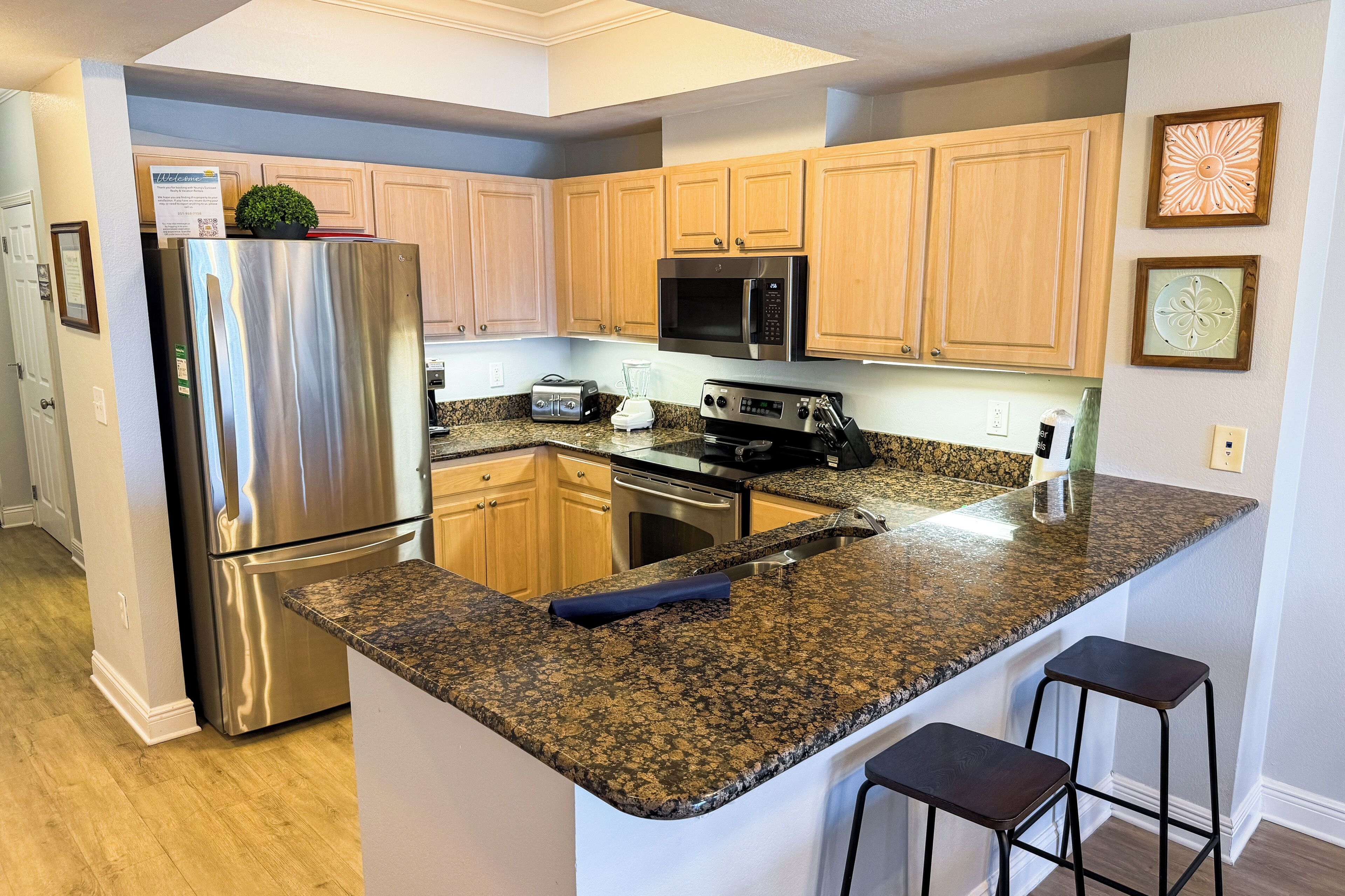 Una cocina con encimeras de granito, electrodomésticos de acero inoxidable, armarios de madera y una isla integrada con taburetes de bar.