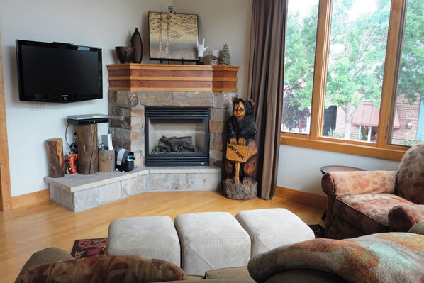 Una sala de estar con chimenea, un televisor montado en la pared y vistas al exterior a través de un ventanal.