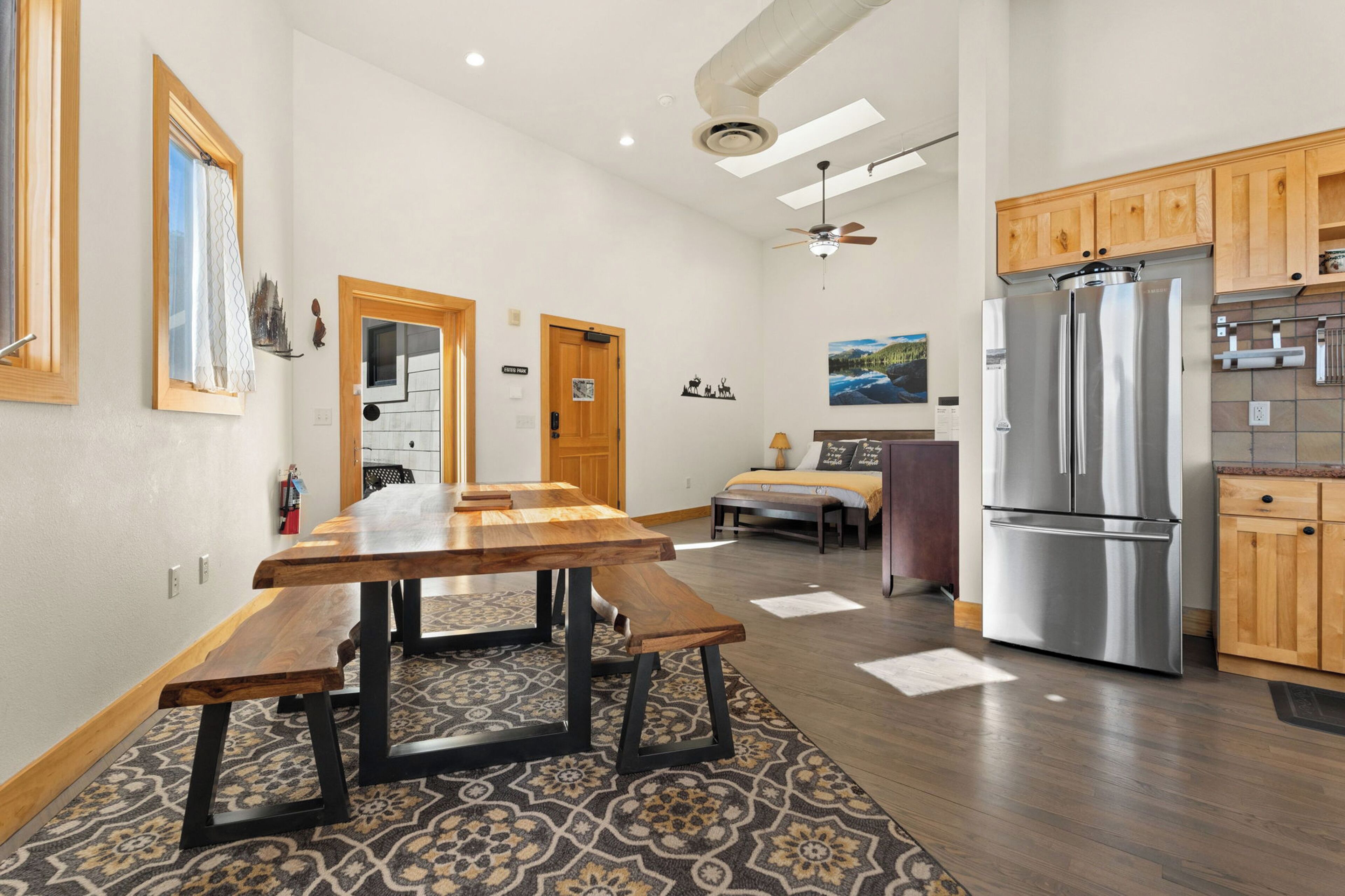 A spacious kitchen with wooden cabinets, a stainless steel refrigerator, and a dining area with a wooden table and benches.