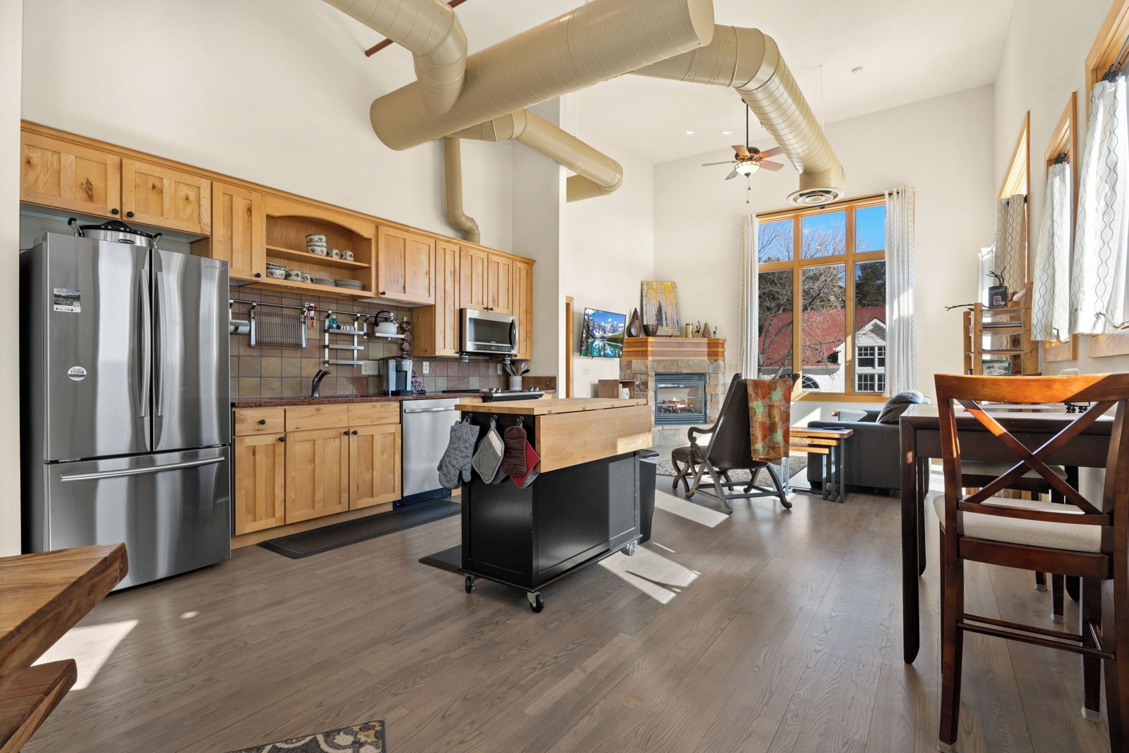 A modern kitchen with stainless steel appliances, wooden cabinets, and a large window overlooking a residential area.