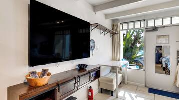 Ein modernes Wohnzimmer mit großem Flachbildfernseher, Holzkonsole, weißem Sofa und einem Fenster mit Blick auf Grünflächen.