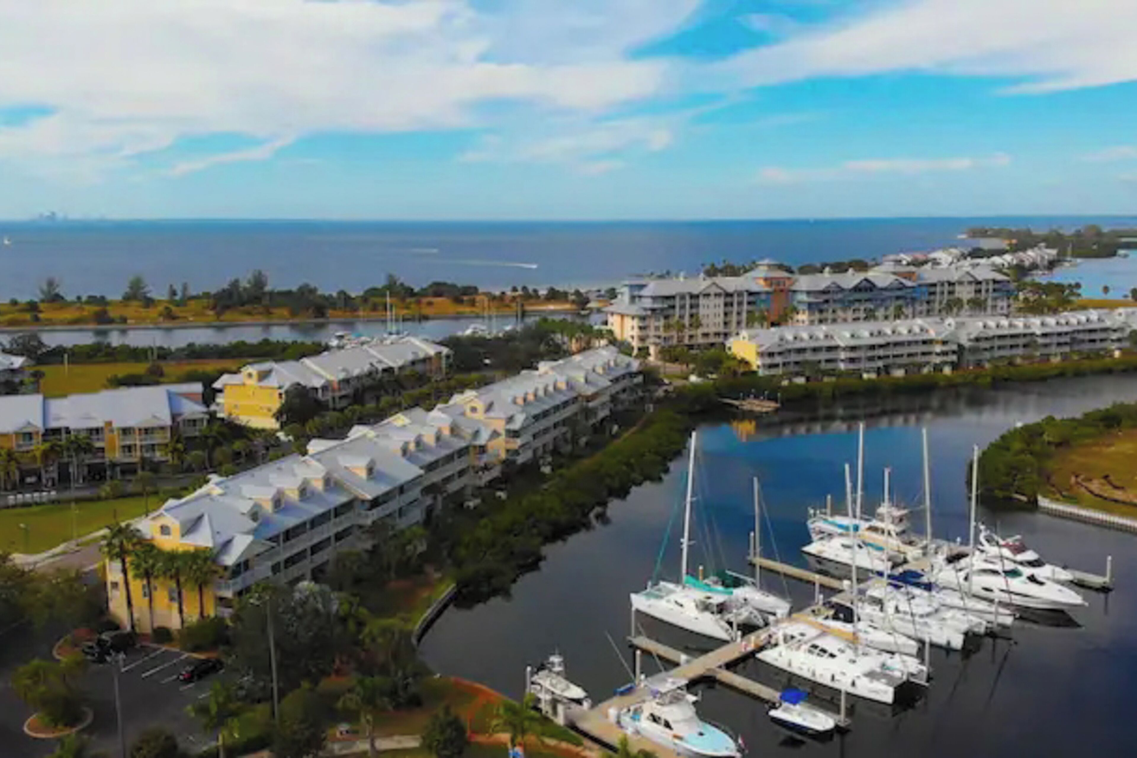 Un puerto deportivo con varias embarcaciones amarradas, un hotel con una hilera de edificios y vista al océano.