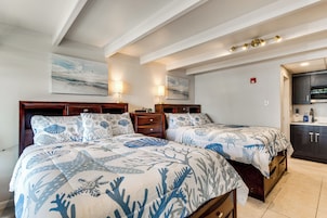 A bedroom with two beds, a wooden headboard, a nightstand, a wall-mounted lamp, and a painting.