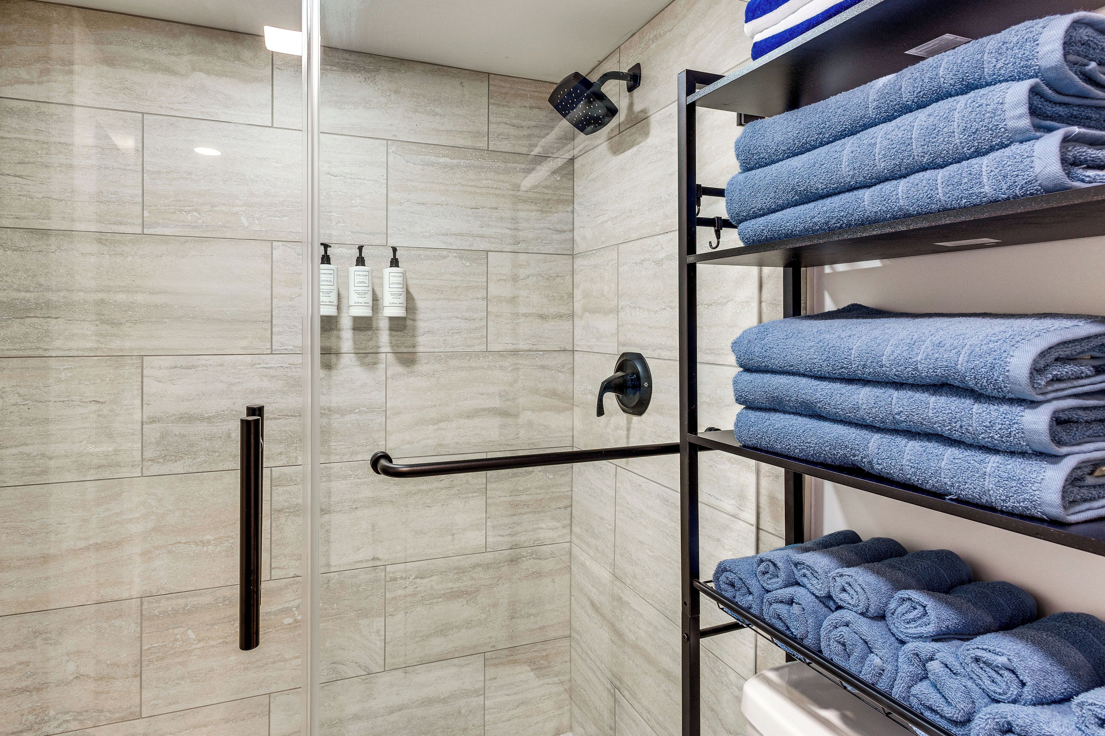 A modern bathroom with a glass shower enclosure, a towel rack with folded towels, and toiletries on the wall.