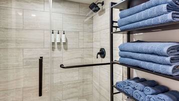 A modern bathroom with a glass shower enclosure, a towel rack with folded towels, and toiletries on the wall.
