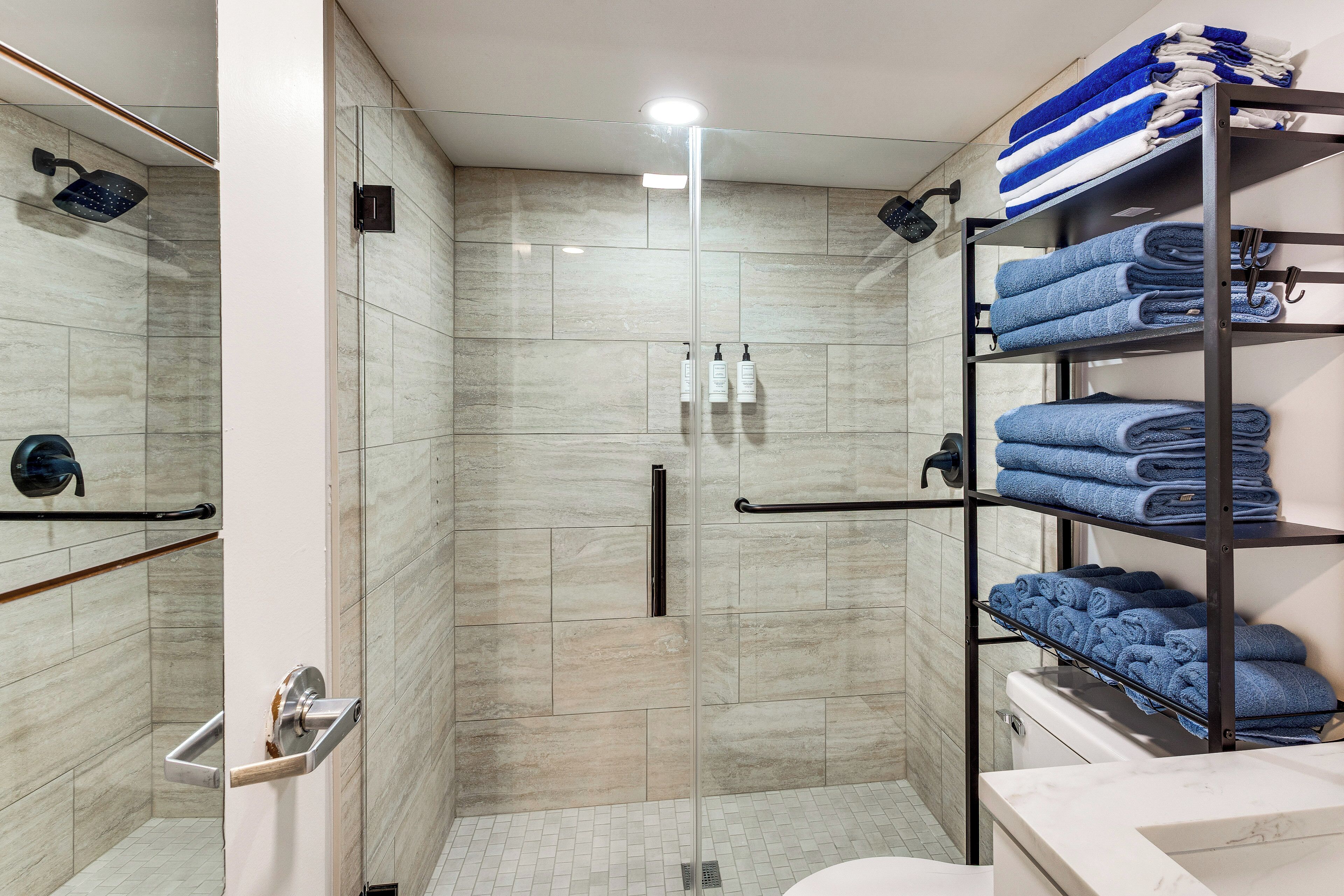 A modern bathroom with a glass-enclosed shower, a towel rack with folded towels, and a toilet.