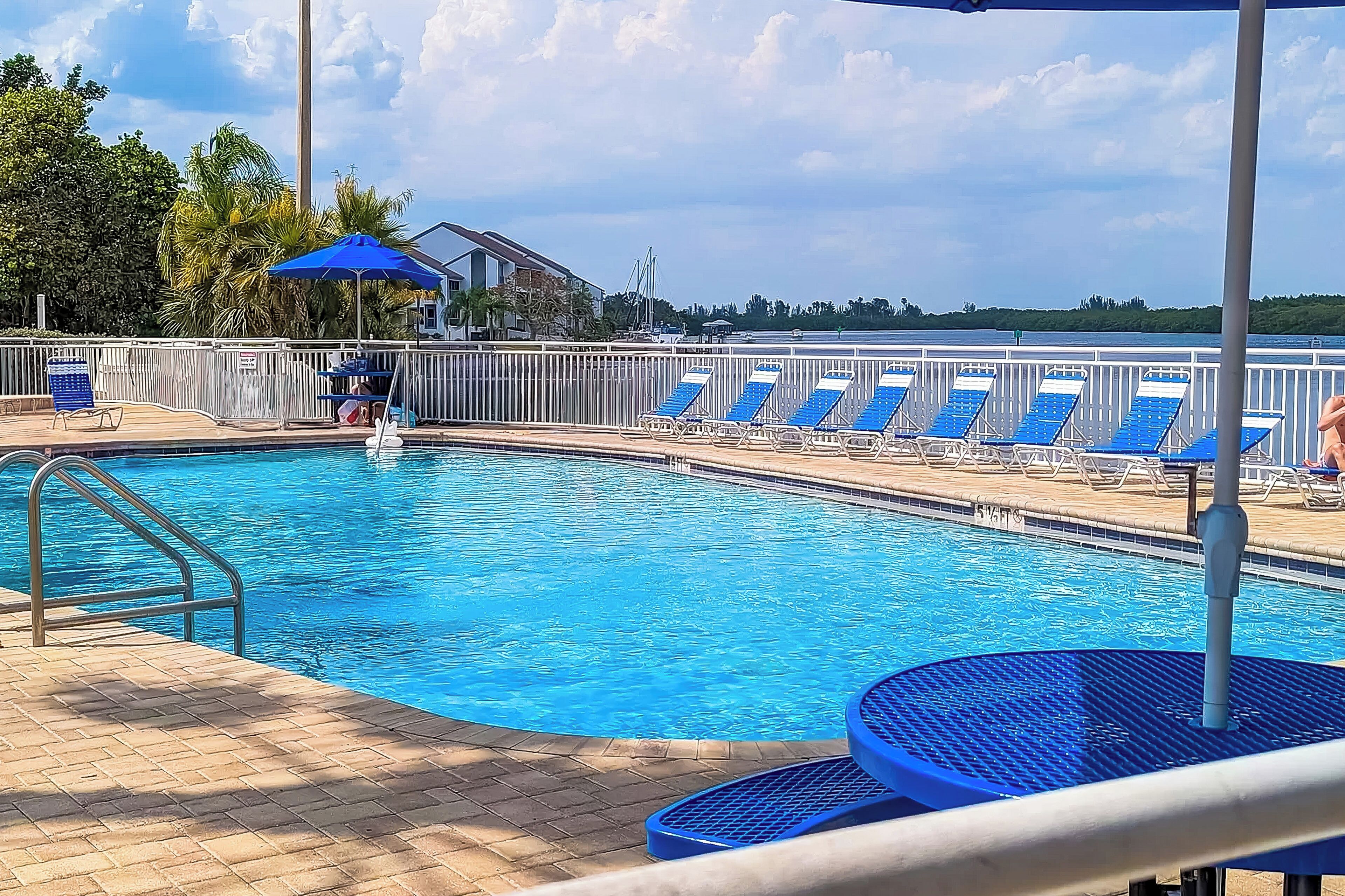 Piscina com cadeiras azuis e área coberta com guarda-sol.