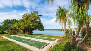 A green shuffleboard court surrounded by lush greenery and palm trees, with a body of water in the background. - Dolphin & Manatee Cove Condo: Beach Access + More! (Ruskin)